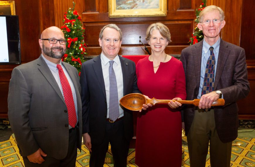 Ara, Alex, Wendy, and Charley stand in front of a Christmas tree holding a large wooden spoon.