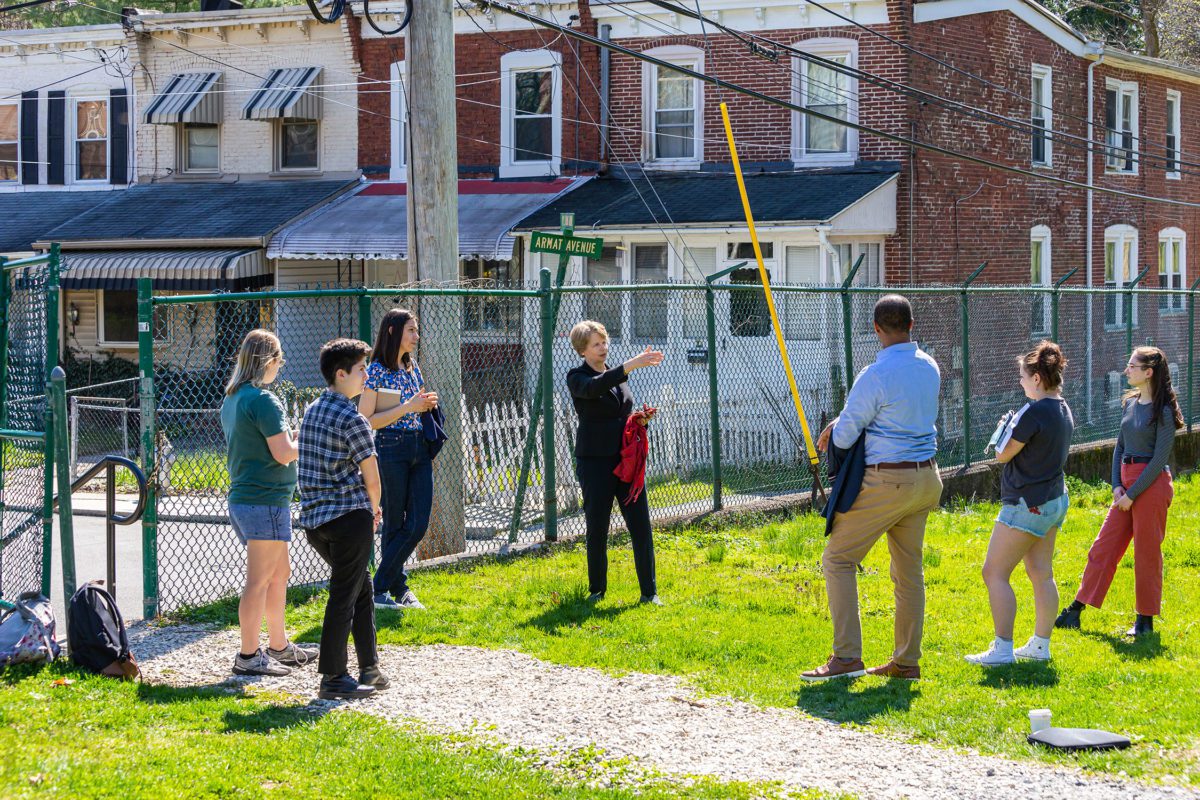 Four students, Farneth, Raymond, and McKnight stand in from tof the chain link fence on the border of Haverford and Ardmore with twin homes visible behind it.