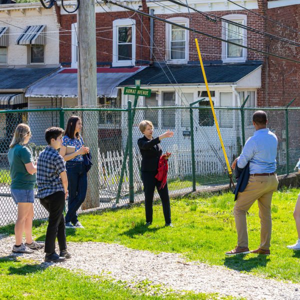 Four students, Farneth, Raymond, and McKnight stand in from tof the chain link fence on the border of Haverford and Ardmore with twin homes visible behind it.