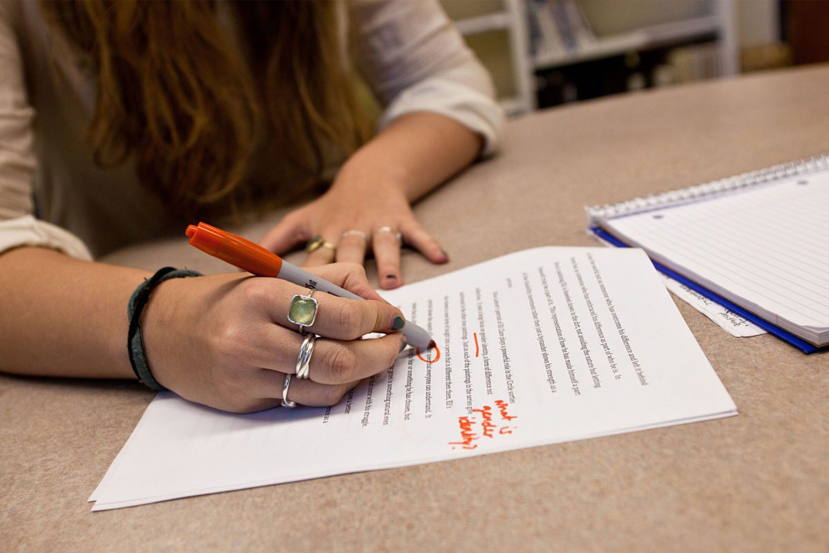 A close-up photo of a hand marking up a paper with a red pen.