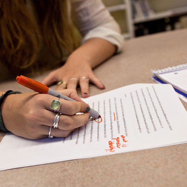 A close-up photo of a hand marking up a paper with a red pen.