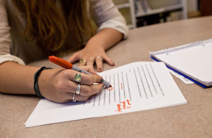 A close-up photo of a hand marking up a paper with a red pen.