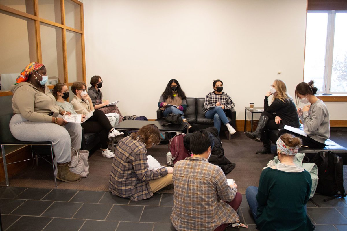 10 masked students and their professor sit in a circle in chairs and on the floor outside the gallery in Whitehead Campus Center