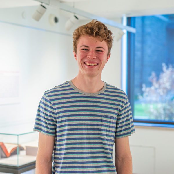 Nick wears a striped shirt and smiles in the gallery in the library.