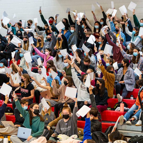 Students wearing masks and seated in the GIAC hold up packets to vote at plenary