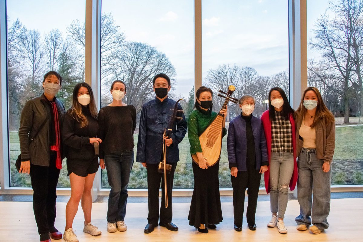 Eight masked people stand in front of a wall of windows in the concert hall, two of whom are holding a erhu (a two-stringed fiddle) and pipa (lute).