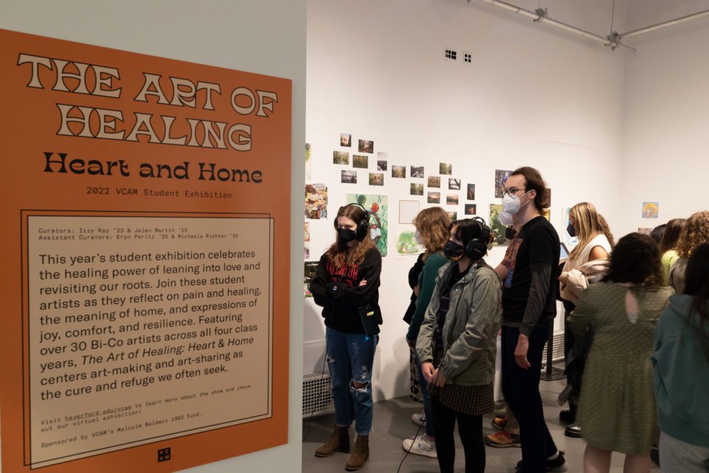 Many masked students in the gallery admiring the art, standing next to the poster for The Art of Healing, which notes that over 30 Bi-Co artists across all four class years contributed work to this exhibit.