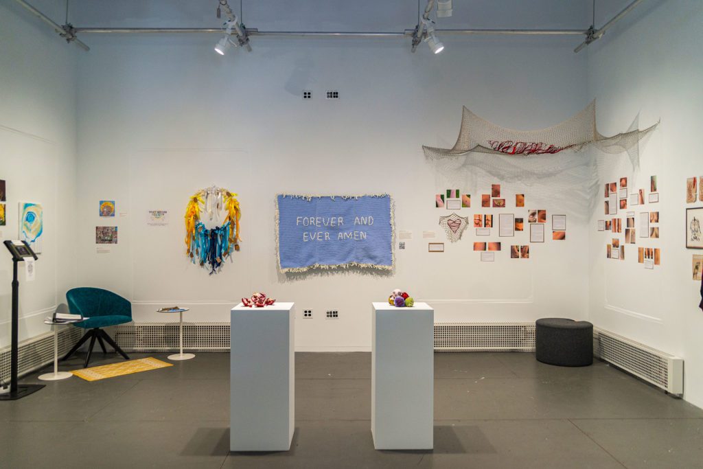 A wide vide of the back wall of the exhibit with several hanging fabric works, including a netting in the corner that looks like sutures.
