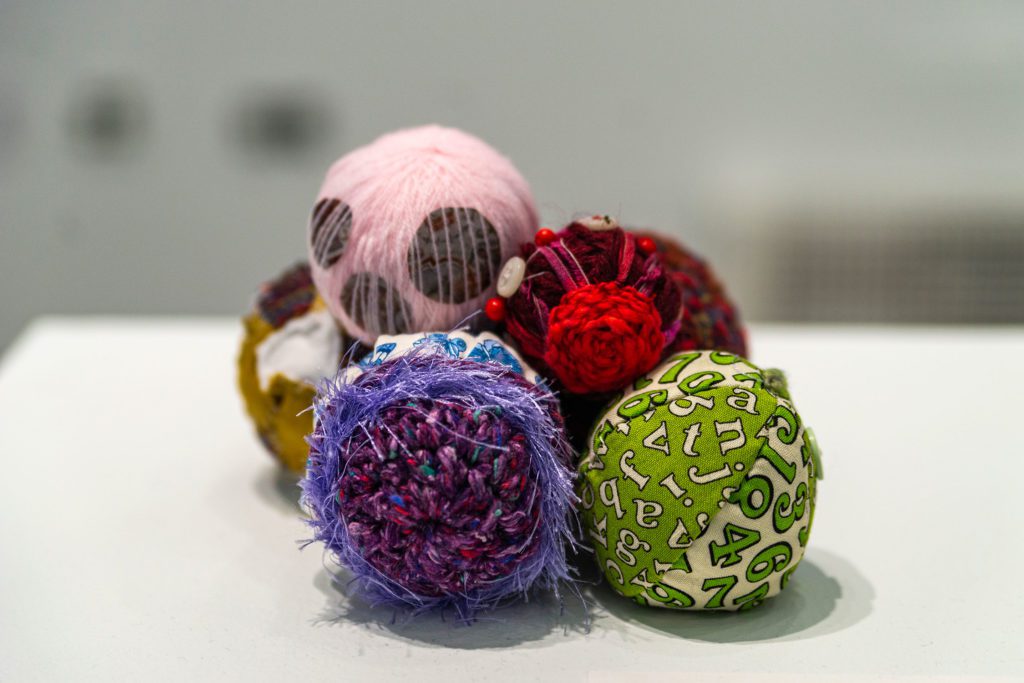 Six differently colored balls of yarn, embroidered with buttons and feathers