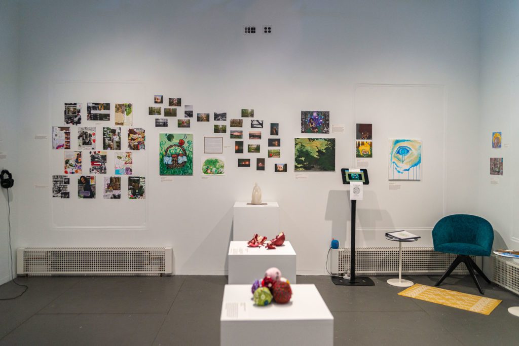 A view of a wall of the gallery filled with 44 different photos, paintings, and drawings of different sizes hanging on it.