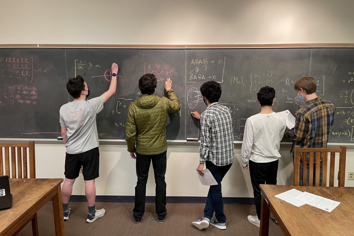 Five students stand in front of a chalkboard working on math problems together.