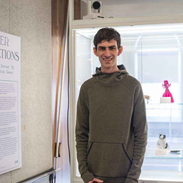 Chris stands in front of the display case with the origami red violinist particularly prominent behind him.