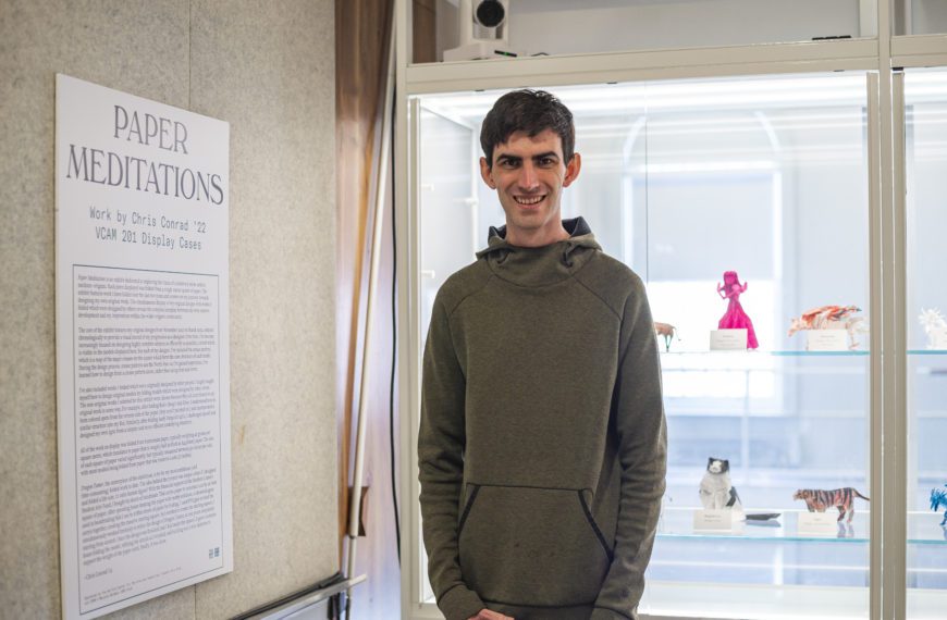 Chris stands in front of the display case with the origami red violinist particularly prominent behind him.