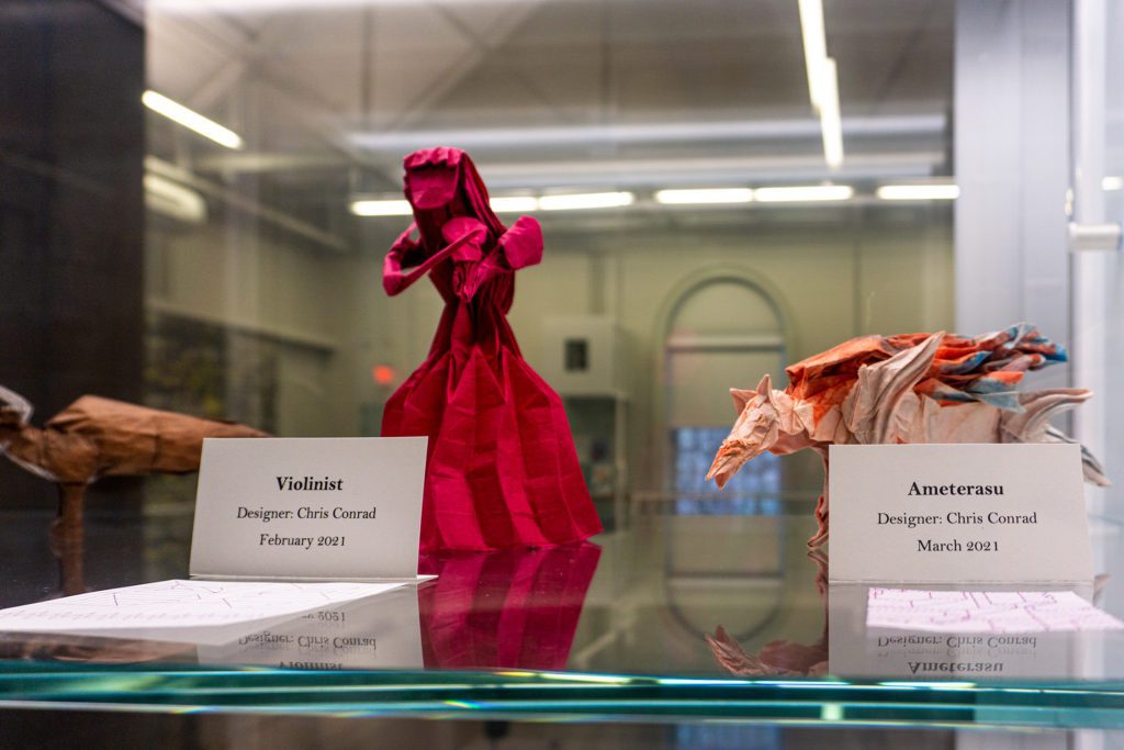 A dramatic red paper violinist next to a paper sculpture of a dragon.