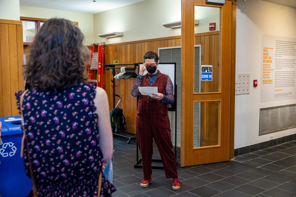 Vicky wears a mask and glasses and reads from a piece of paper at the entrance to the gallery.