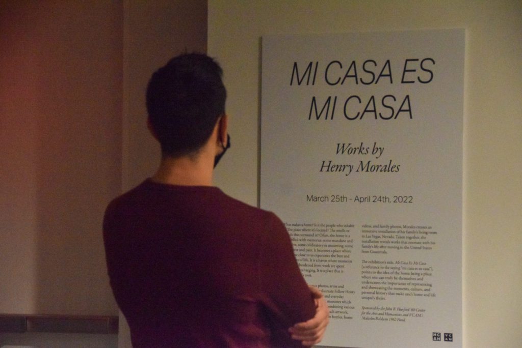 A gallery attendee reads the wall description of "Mi Casa Es Mi Casa"