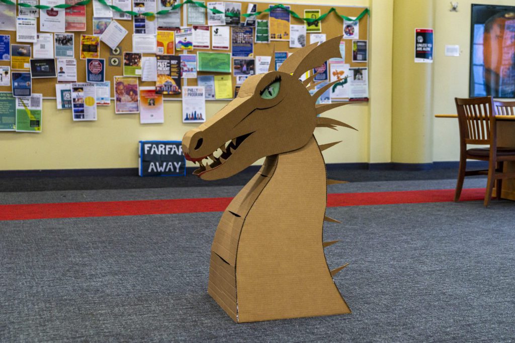 A cardboard dragon head with green eyes sits in Zubrow Commons.