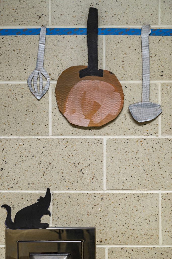 Cutouts of Remy the Rat and his kitchen utensils hang on the wall.
