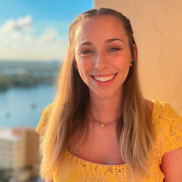 Hannah Roth smiles for the camera with a wall, a river, and trees in the background