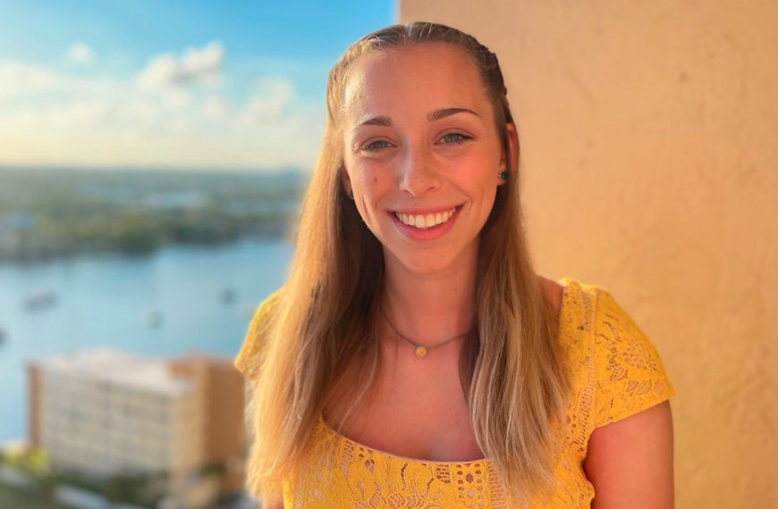 Hannah Roth smiles for the camera with a wall, a river, and trees in the background