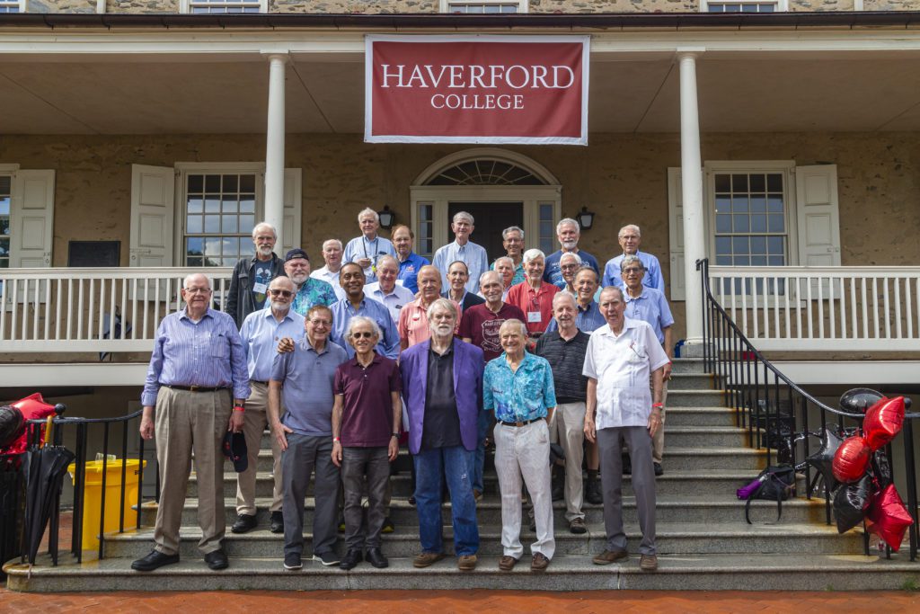 About 25 members of the Class of 1967 pose on the steps of Founders Hall under a red Haverford College banner.