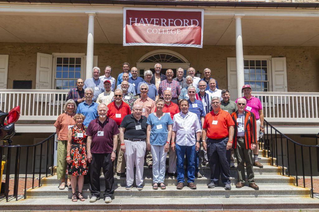 About 30 members of the Class of 1972 pose on the steps of Founders under a red Haverford College banner.