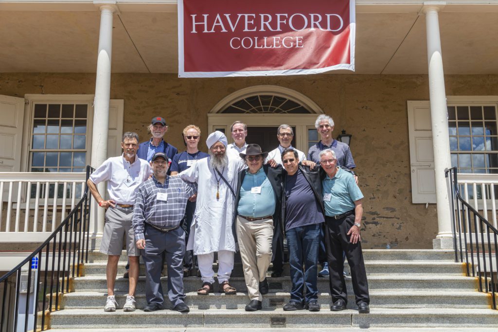 11 men from the Class of 1977 pose with their arms around each other under a red Haverford College banner.