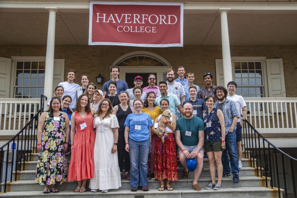About 30 people pose on the steps of Founders under a Haverford College banner. The woman in the center on the front step holds up a small fluffy dog.