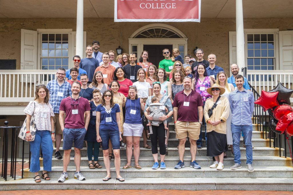 Roughly 40 people pose on Founders steps, many wearing sunglasses and several holding babies and young children.