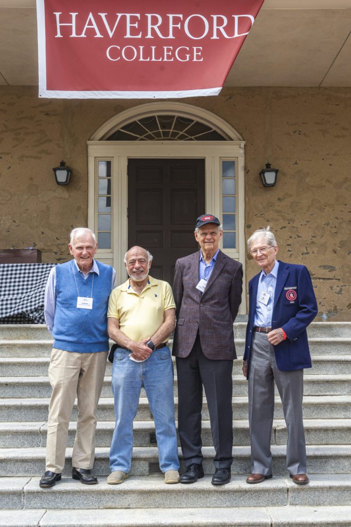 Four members of the Class of 1957 pose on the stairs together under a Haverford College banner.