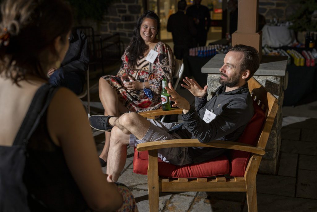 Three alumni sit outside chatting and smiling at night.