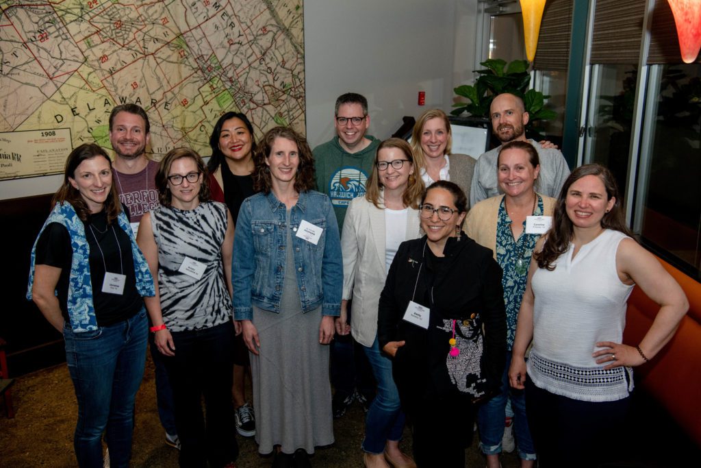 12 members of the Class of 2002 pose together smiling in front of a large map.