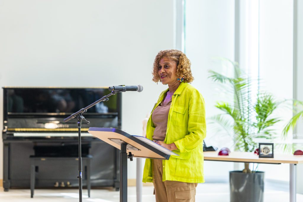 Beverly Ortega Babers '84 wears bright yellow-green and speaks at a microphone in the light-filled concert hall.