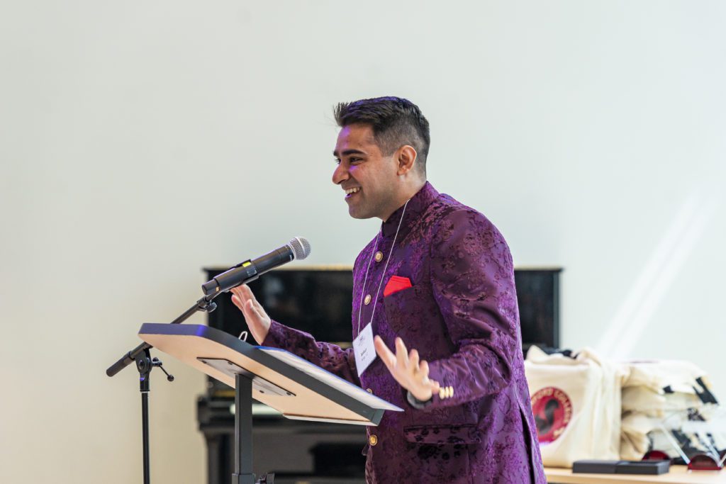 Ankur Arya '12 wears a vibrant purple suit and gestures with his hands during his speech.