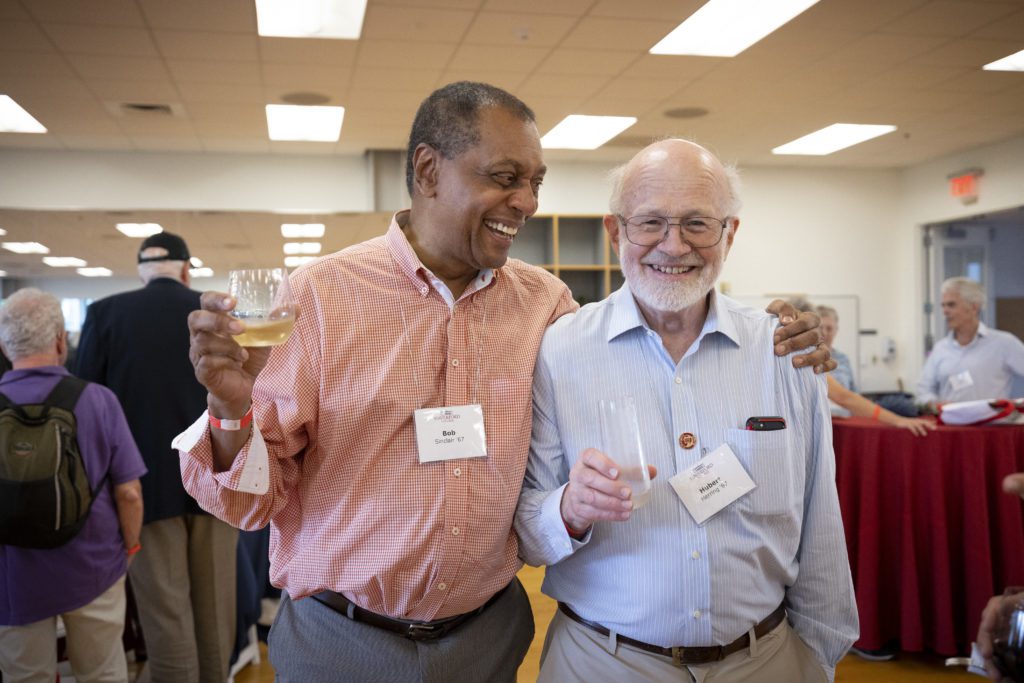 Two alumni put their arms around each other, smiling, each holding a champagne flute