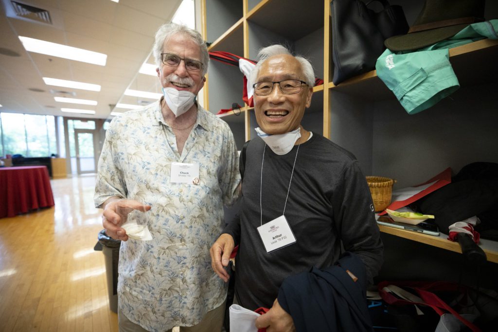 Two friends smile with their masks pulled down and empty champagne classes in their hands.