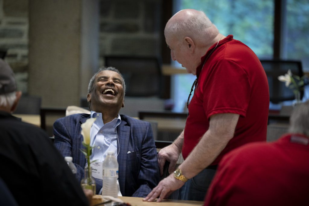 A man throws his head back laughing while talking to another friend.