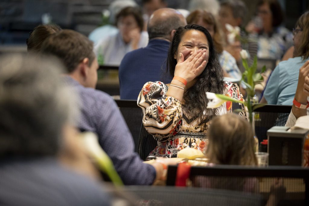 Covering her mouth while laughing at a friend, a woman sits at a table in the DC.
