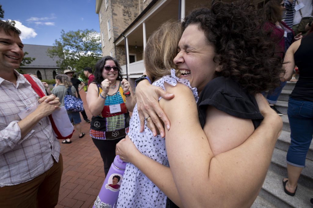 A very excited hug while two friends cheer them on.