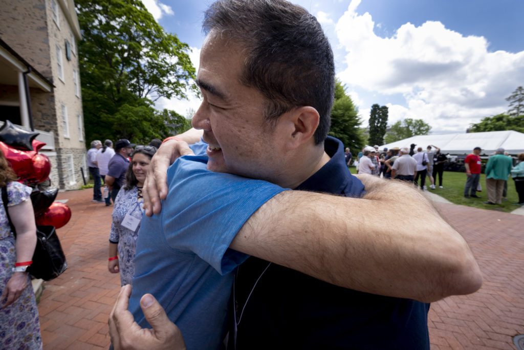 Two friends embrace on Founders Green with blue skies behind them.