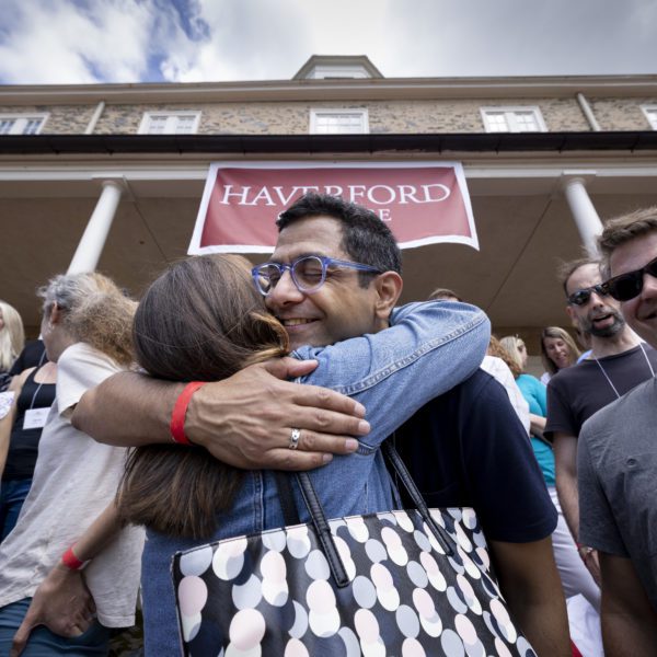Two alumni hug with Founders Hall and its cupola in the background.