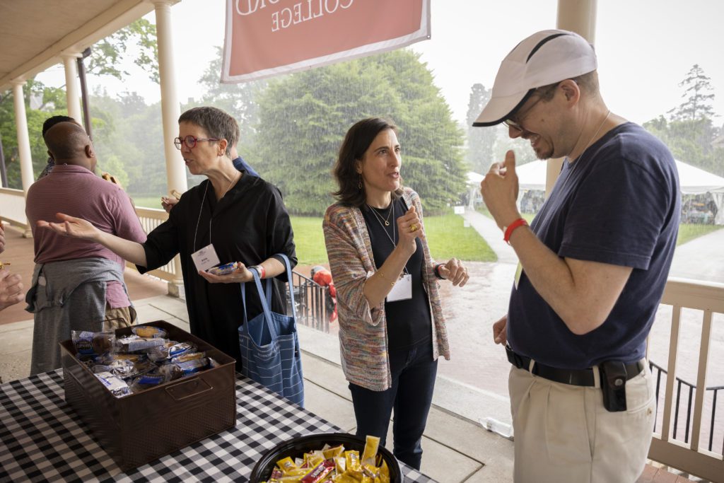 With the pouring rain in the background, four alumni chat and eat snacks on the porch.