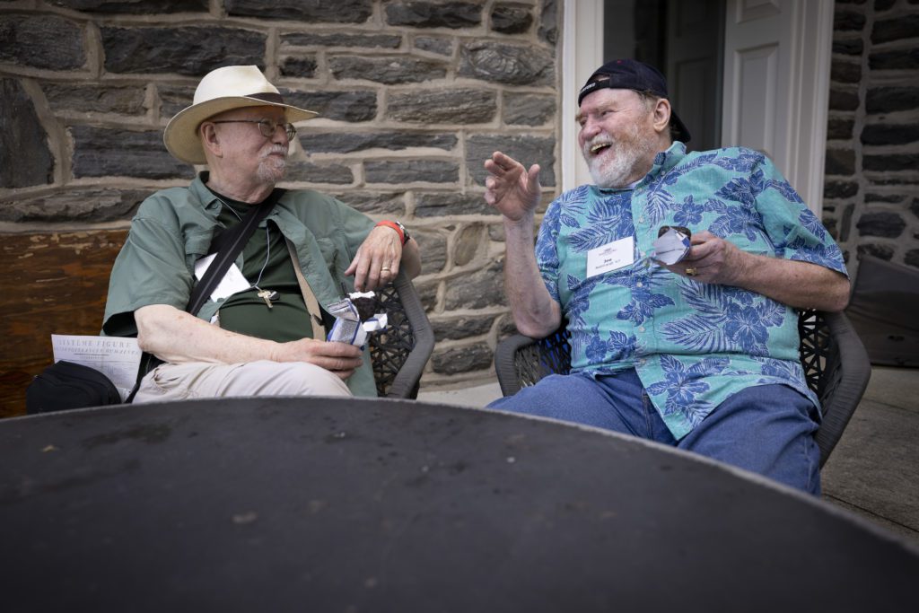 Two alumni wearing hats sit and eat ice cream on VCAM patio