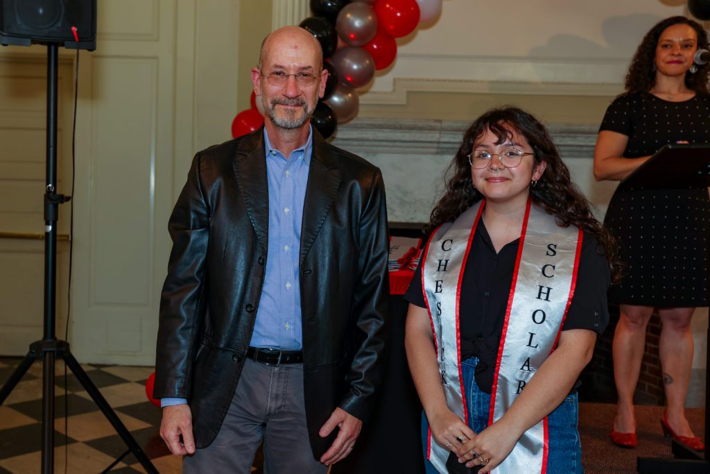 Shayleah Jenkins poses with Jeff Tecosky-Feldman at the podium after receiving the Chesick sash. Christina Rose stands in the background.