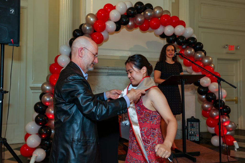 Jeff Tecosky-Feldman reaches over Annette Lee's shoulders to put on her Chesick Scholar sash