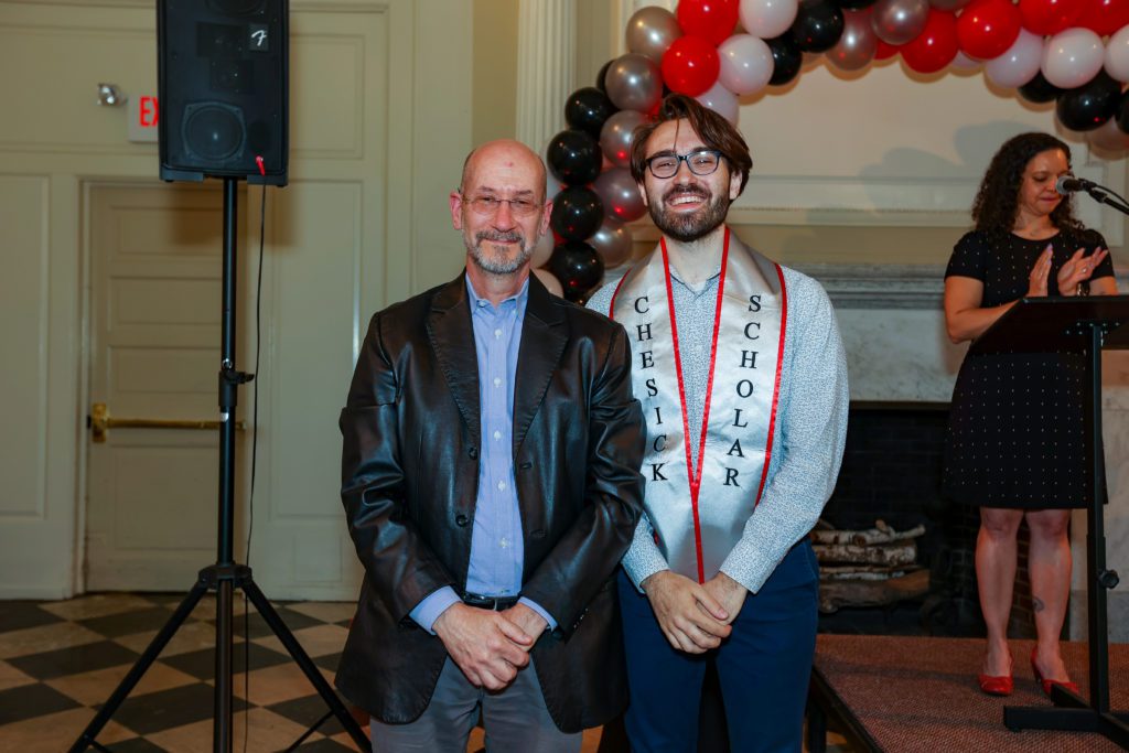 Jacob Valero smiles next to Jeff Tecosky-Feldman with Christina Rose and a black, gray, red, and white balloon arch in the background