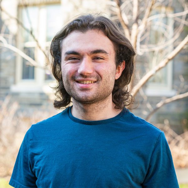 Joshua Bayona '22 stands in front of a tree on Haverford's campus, smiling.