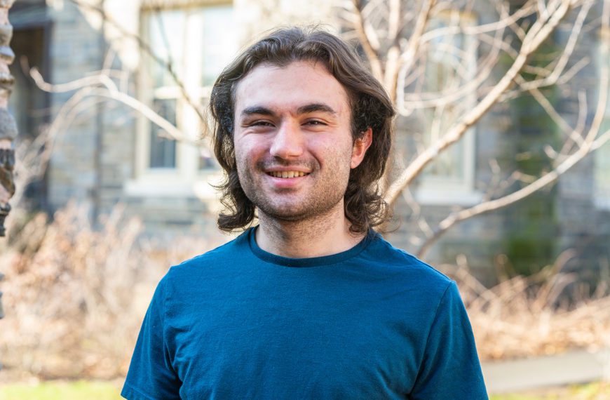 Joshua Bayona '22 stands in front of a tree on Haverford's campus, smiling.