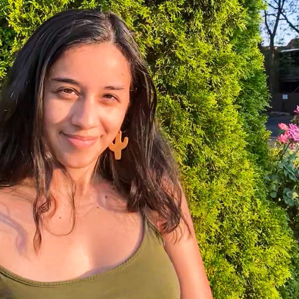 Sam Olivares-Mejia stands in front of a green bush, smiling.