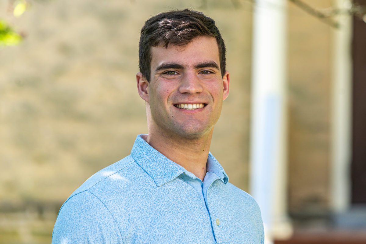 Nathaniel Ruhl stands in front of a wall, smiling.